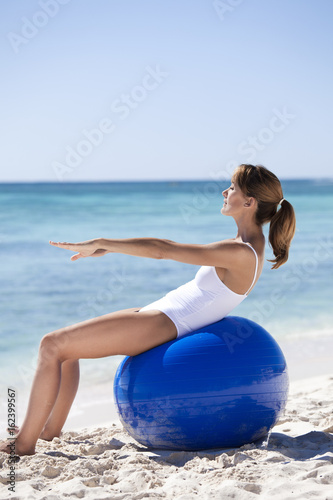 femme sur la plage qui fait des abdominaux sur une balle de gymnastique