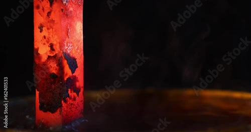  Close-up of blacksmith cooling a iron rod in water at workshop