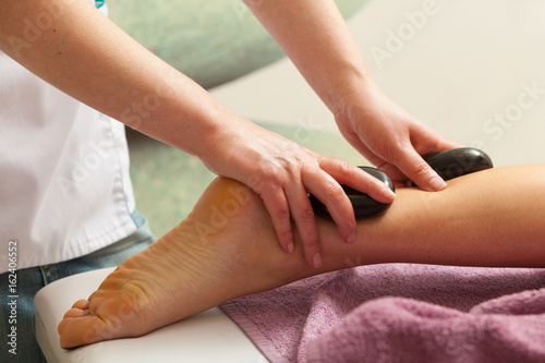 Masseuse doing legs massage with hot stones