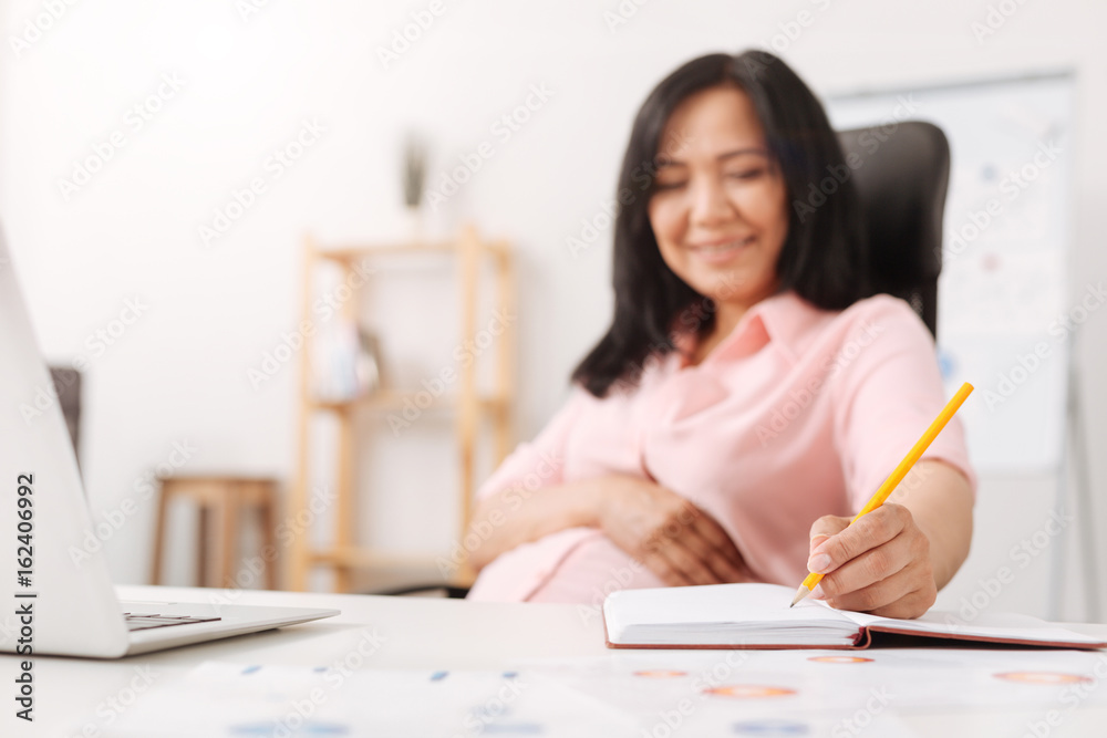 Cheerful pregnant woman making notes in the office Cheerful pregnant woman making notes in the office
