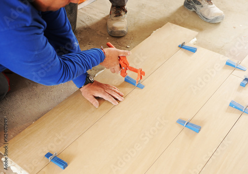 Foto Bricklayer placing a porcelain stoneware floor with special tools, plastic tongs