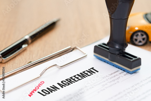 Approved loan agreement document with rubber stamp and car model toy on wooden desk.
