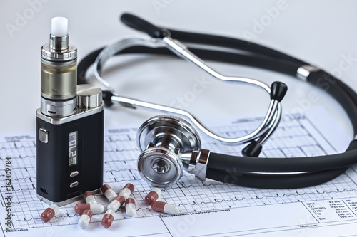 Freigestellte E-Zigarette mit einem Stethoskop und Medikamentenkapseln auf einem weißen EKG-Ausdruck