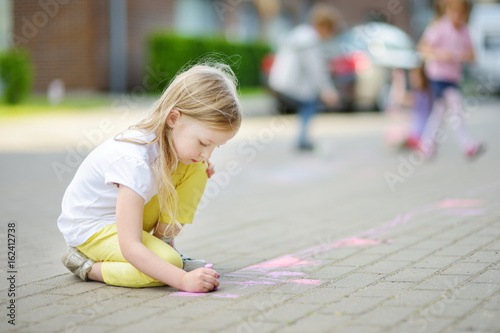 Cute little girl drawing with colorful chalks on a sidewalk. Summer activity for small kids.