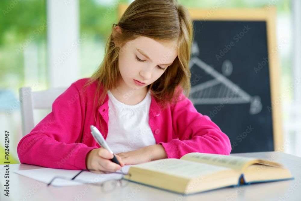 Smart little schoolgirl with pen and books writing a test in a classroom. Child in an elementary school. Smart little schoolgirl with pen and books writing a test in a classroom. Child in an elementary school.
