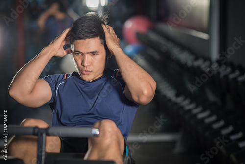 Asian man doing sit-ups at gym.