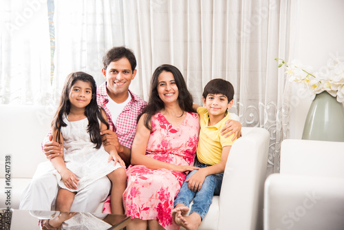 Photography Candid Portrait of smart indian family of four while sitting on sofa