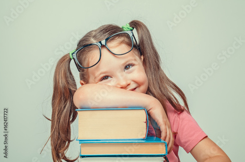 Fotografiet smiling beautiful cute little girl leaning on thick books