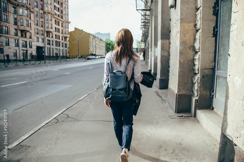 Back view of a hipster girl walking on city street