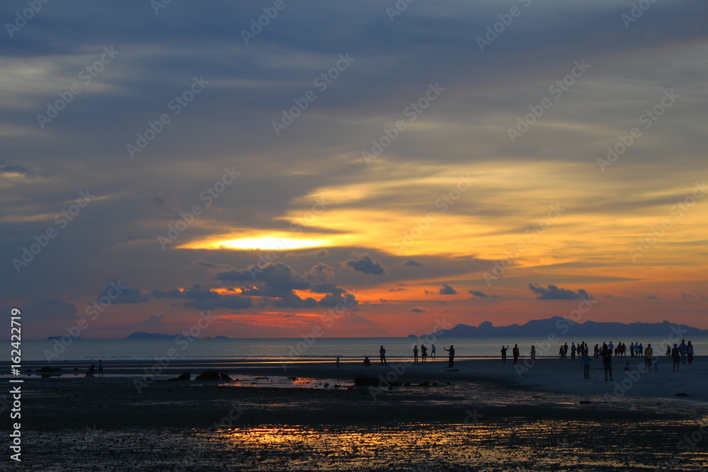Beautiful fiery sunset with people on the seashore with reflection in water