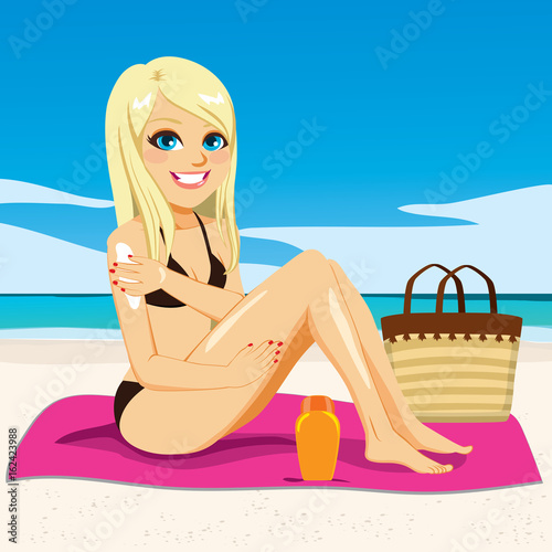 Beautiful young happy blonde woman applying suntan cream on her arms sitting in pink towel at beach sunbathing