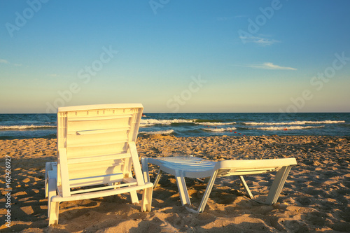 Two deckchairs on the beach with bright sun and waves © pilat666