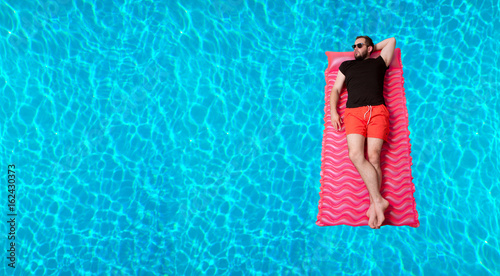 Man in t-shirt and shorts on inflatable mattress in the swimming pool.