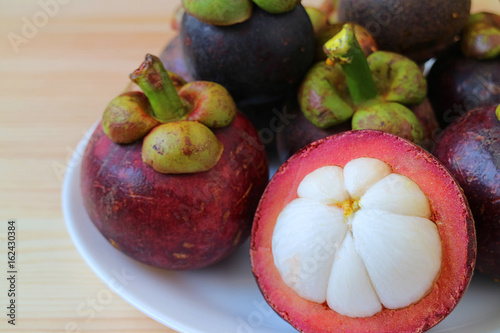 Ripe Purple Mangosteen Whole Fruits and Opened to Show tasty Pure White Meat on a Plate