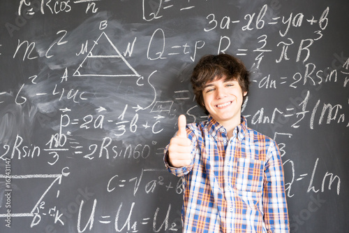 Teenage Boy showing thumb up finding idea with complicated math formulas on black board
