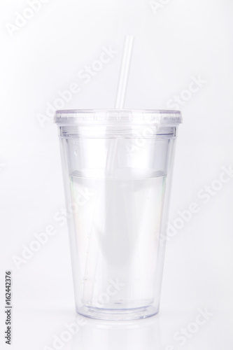 Clear plastic tumbler glass with lid and straw on a white surface. Travel cup isolated on white background.