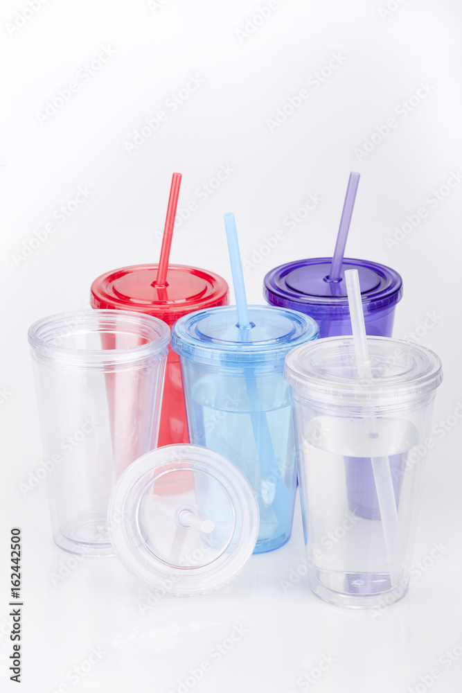 Colorful plastic tumbler glasses with lid and straw on a white surface. Travel cups isolated on white background. Colorful plastic tumbler glasses with lid and straw on a white surface. Travel cups isolated on white background.