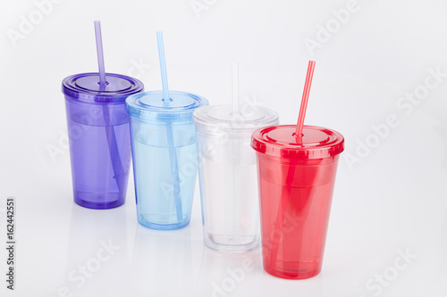 Colorful plastic tumbler glasses with lid and straw on a white surface. Travel cups isolated on white background.