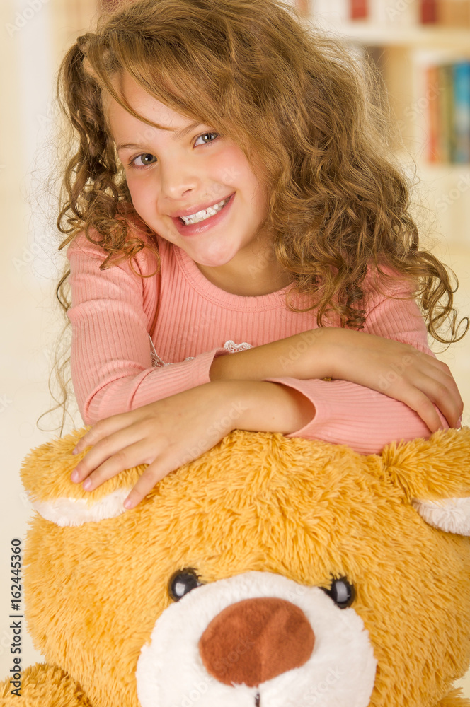 A portrait of a young pretty girl smiling and posing over her teddy bear s  head in a doctor office background Stock Photo