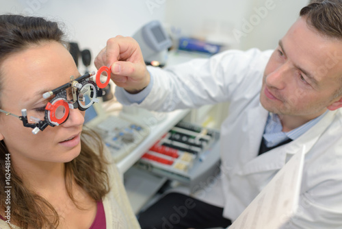 optometrist examining young female patient on phoropter photo