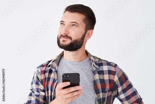 Pensive bearded man looking upward while texting on telephone