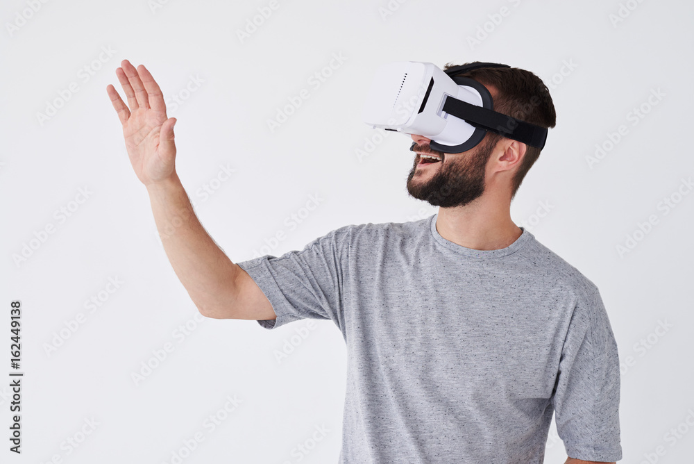 Smiling bearded man using VR glasses trying to touch objects in virtual reality