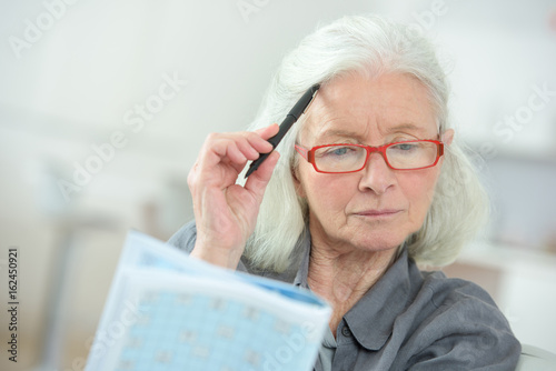 Cuadro en lienzo senior woman sitting at a table completing a crossword puzzle