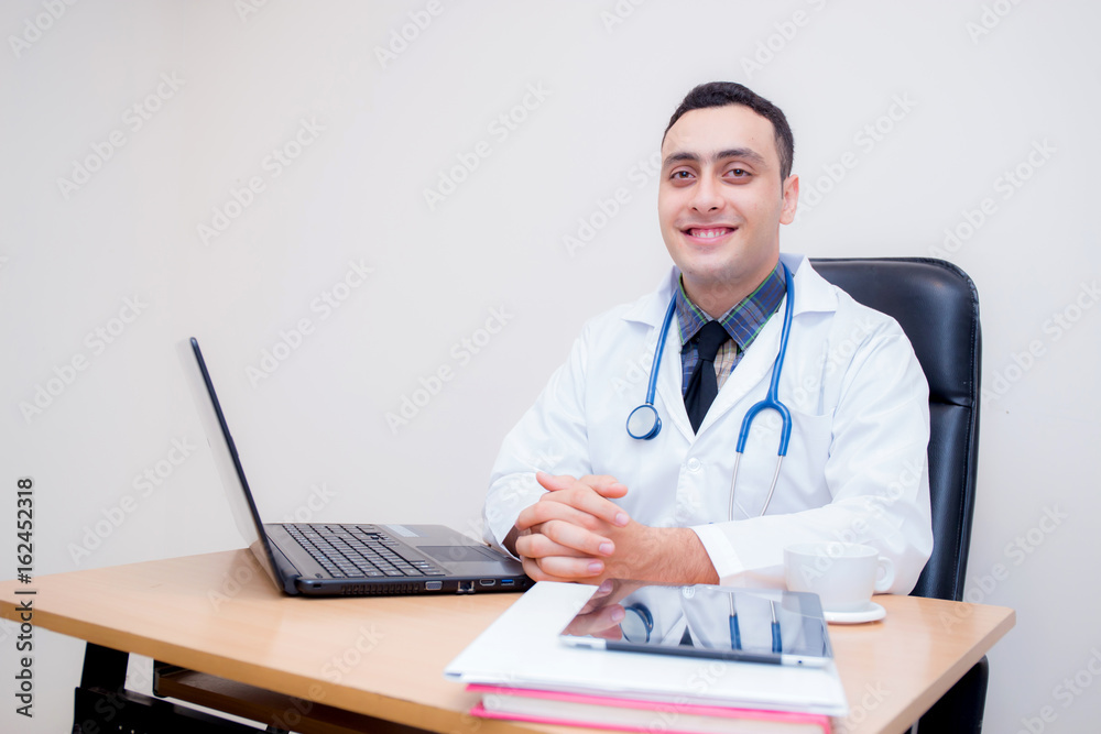 confident male doctor sitting at office desk and smiling, medical healthcare concept. confident male doctor sitting at office desk and smiling, medical healthcare concept.