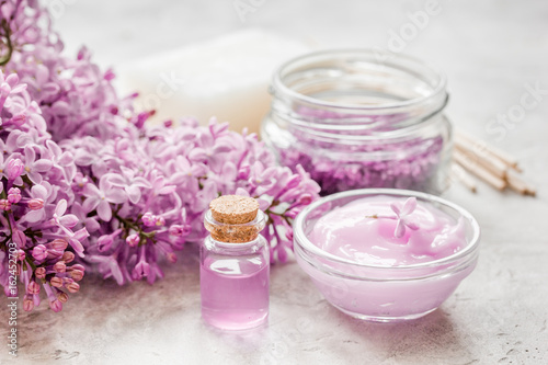 organic salt, cream, extract in lilac cosmetic set with flowers on stone table background