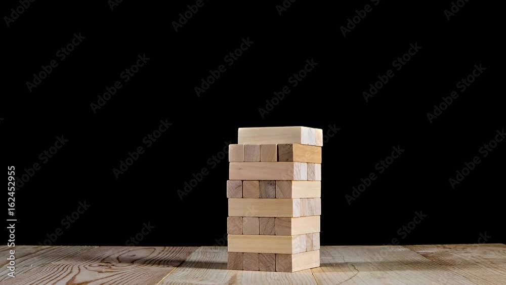 Wooden puzzles jenga gather in tall tower. Stop motion, black background