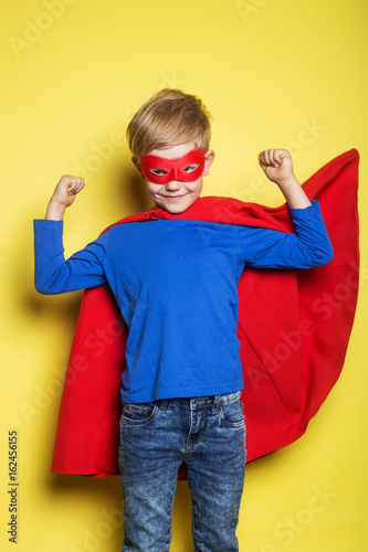 Boy in red super hero cape and mask. Superman. Studio portrait over yellow background