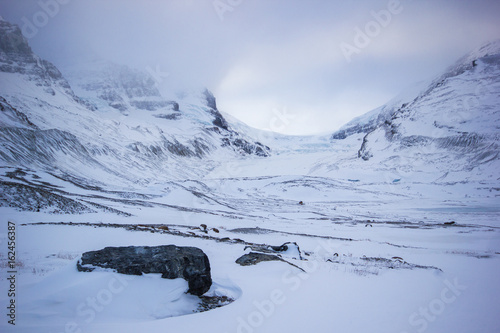 Fotografie Ice and rocks slowly melting from huge athabasca galcier under cloudy sky, Banff
