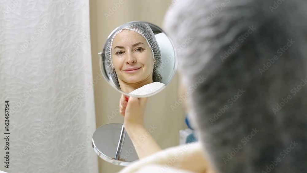 Beautiful woman looks at herself in mirror after cosmetic procedures in the beauty salon Beautiful woman looks at herself in mirror after cosmetic procedures in the beauty salon