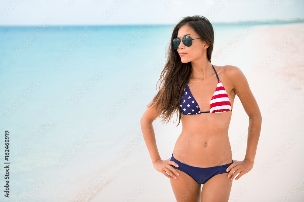 American USA flag bikini girl beach party vacation on summer holidays. Sexy Asian woman with slim body wearing fashion swimsuit for 4th of July independence day celebration.