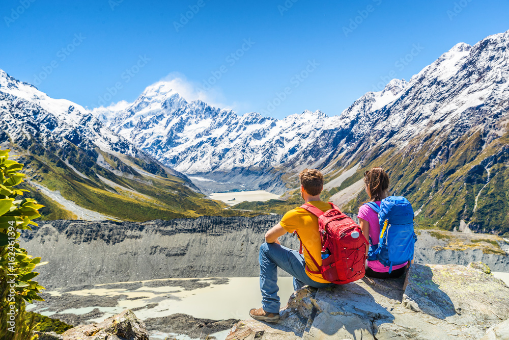 Fototapeta premium Backpackers couple hiking looking at Mount Cook view on mountains tramping in New Zealand. People hikers relaxing during hike in alps of south island.