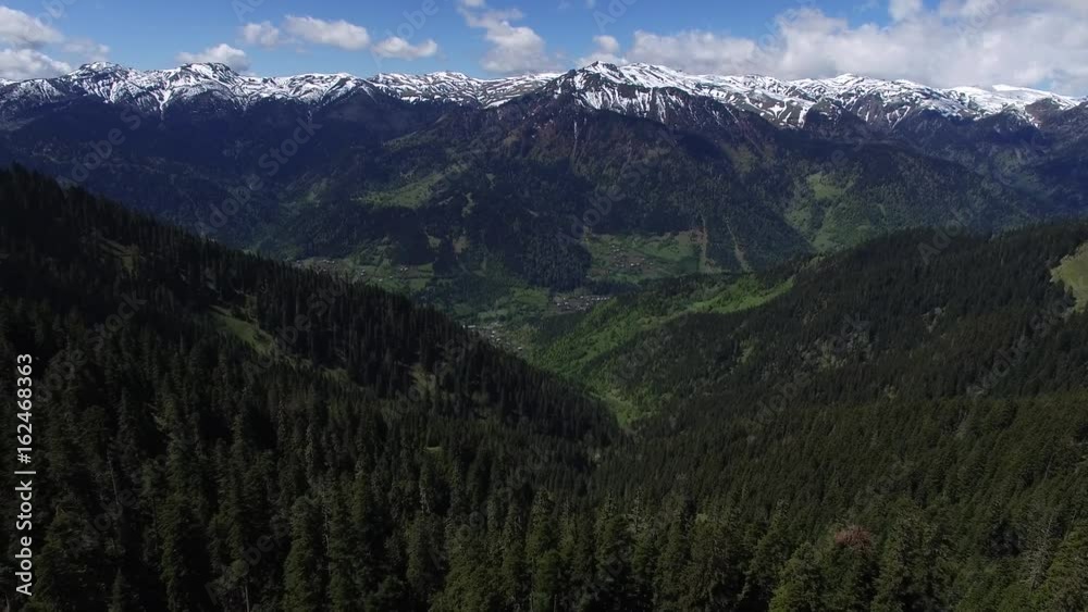 Mountain panorama on a sunny day. Aerial view of the slopes covered with coniferous forest, small villages in the valleys, a pastures and a mountain ranges on the horizon. Georgia. Mountain panorama on a sunny day. Aerial view of the slopes covered with coniferous forest, small villages in the valleys, a pastures and a mountain ranges on the horizon. Georgia.