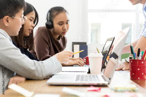 Group of college Asian students looking at laptop computer discussing project