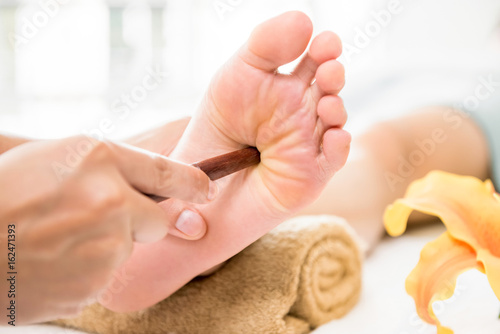 Professional therapist giving traditional thai foot massage with stick to a woman