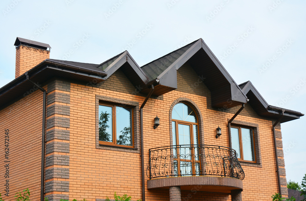 Brick house construction with different types of roof design and metal balcony. Roofing Construction.