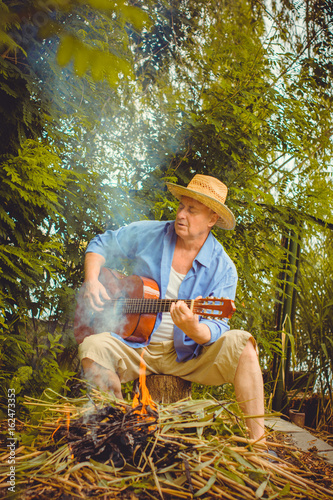 Mature relaxed man playing music on acoustic guitar in a beautiful nature background