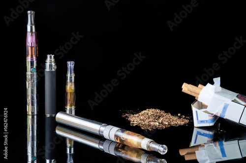 E-cigarette with pile of grinded tobacco leaves and a pack of smokes