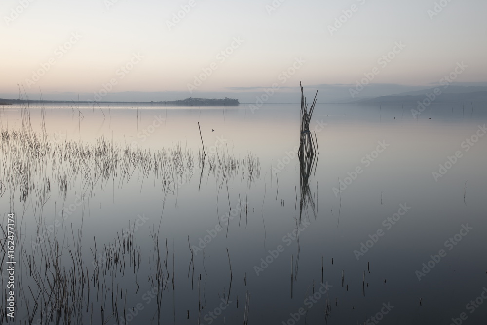 Mininalist view of a lake, with some wooden poles on still water and soft colors