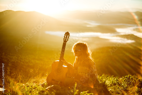 Young girl meets sunrise on top of a mountain with a guitar