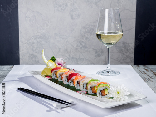 Rainbow sushi roll with salmon and avocado, complete with a glass of white wine