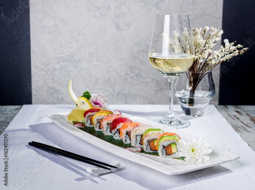 Rainbow sushi roll with salmon and avocado, complete with a glass of white wine and a tempura decoration