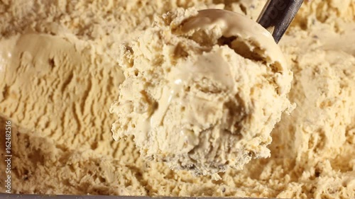 strawberry ice cream scooped out of container spoon is a ball. Close-up of caramel ice cream in a large box. Round spoon makes shoelaces balls for buyers