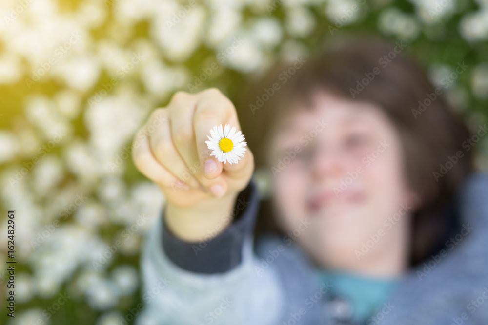Little boy lying and sleeping or dreaming on summer meadow green grass with daisy and holding little white daisy. Attractive smiling teen boy posing over nature background, image toned. Little boy lying and sleeping or dreaming on summer meadow green grass with daisy and holding little white daisy. Attractive smiling teen boy posing over nature background, image toned.