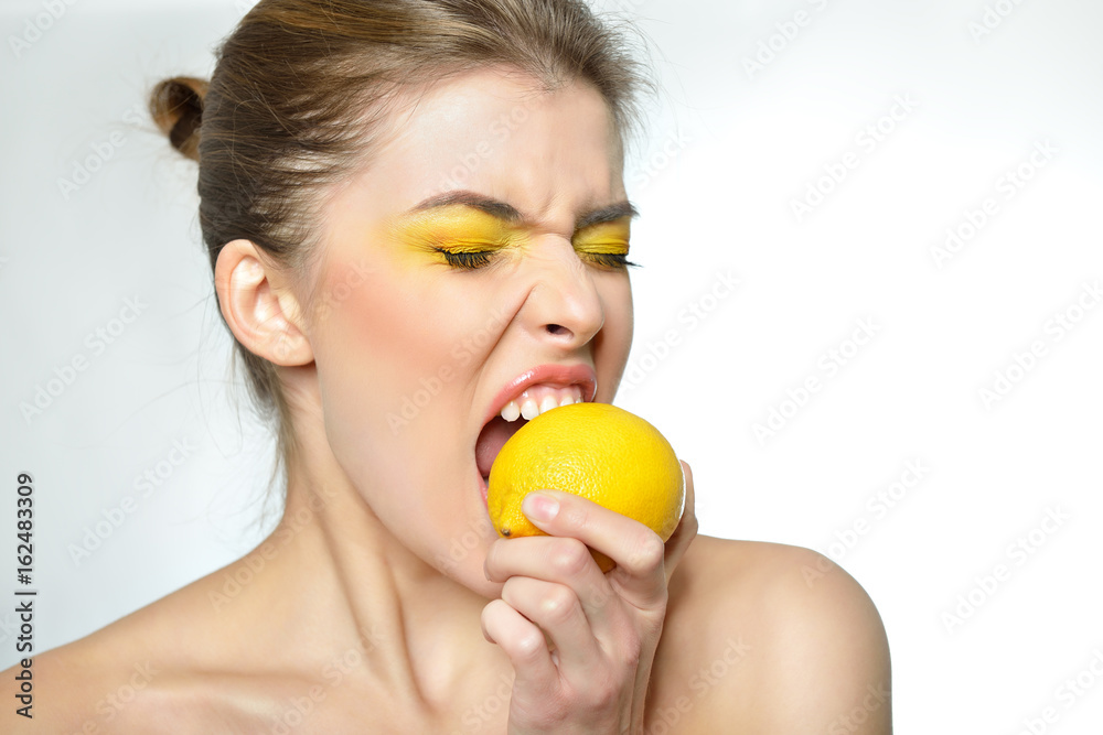 Young attractive girl posing at studio with lemon. Beautiful female face with healthy skin and close eyes. Young woman with vivid makeup eats lemon. Young attractive girl posing at studio with lemon. Beautiful female face with healthy skin and close eyes. Young woman with vivid makeup eats lemon.