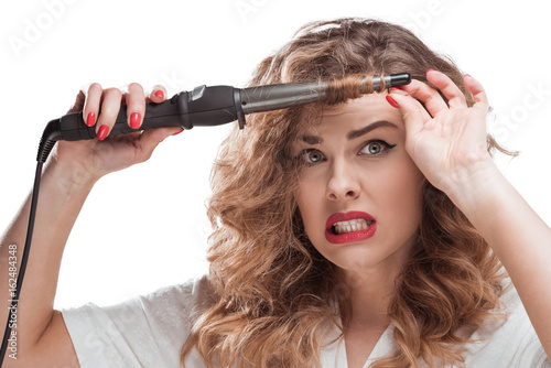 shocked woman with curling iron in hands looking at camera isolated on white