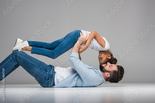 Happy multiethnic father and daughter having fun together on grey